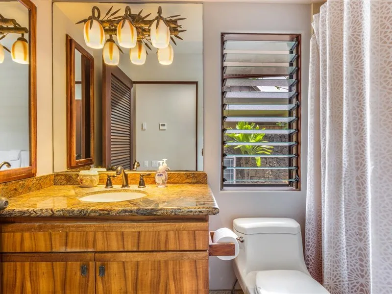 Un tocador de baño con lavabo, espejo e inodoro junto a una ventana.