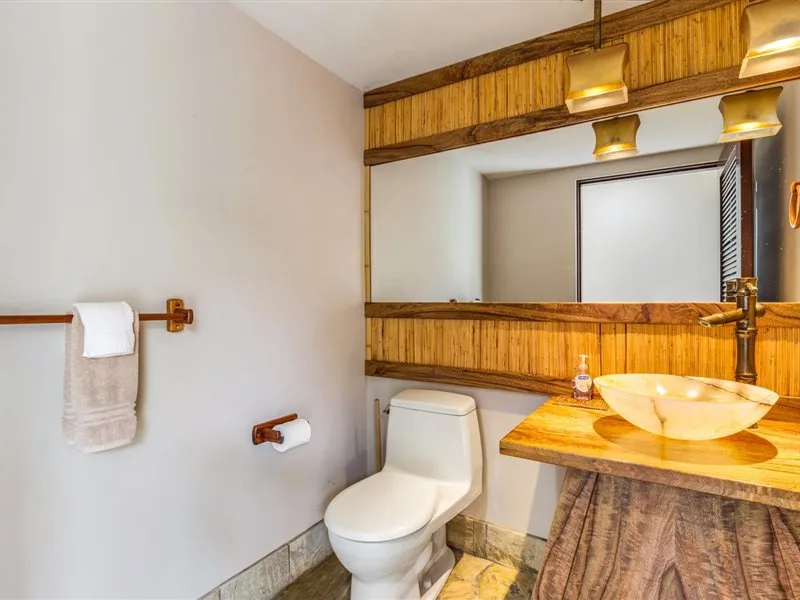 Un baño con inodoro, tocador de tonos madera y lavabo sobre encimera.