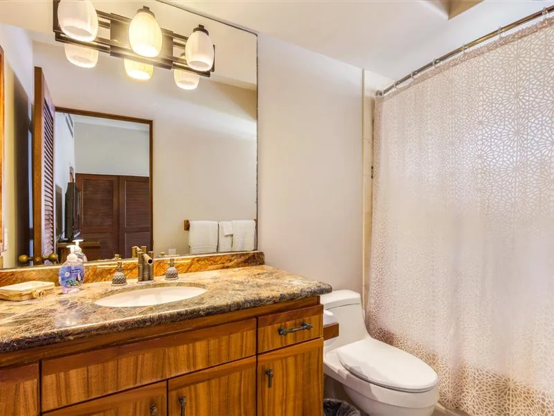Un baño con un tocador largo, espejo y cortina de ducha estampada.