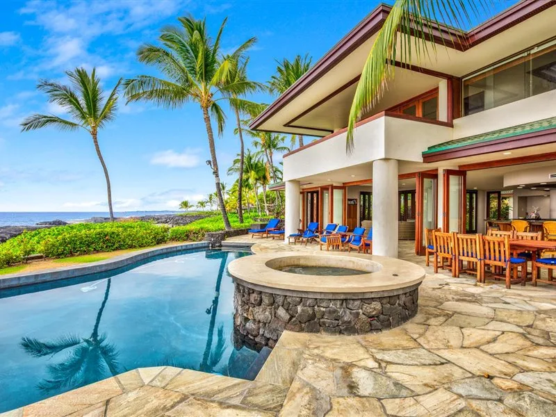 Un patio de una villa costera da a una piscina, con palmeras y asientos al aire libre.