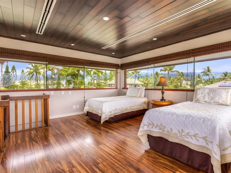 Un dormitorio luminoso con dos camas, grandes ventanas y vistas a palmeras.