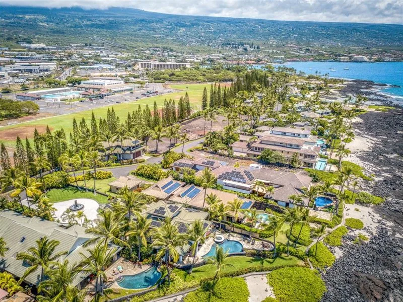 Vista aérea de un complejo turístico costero con piscinas, edificios y jardines.