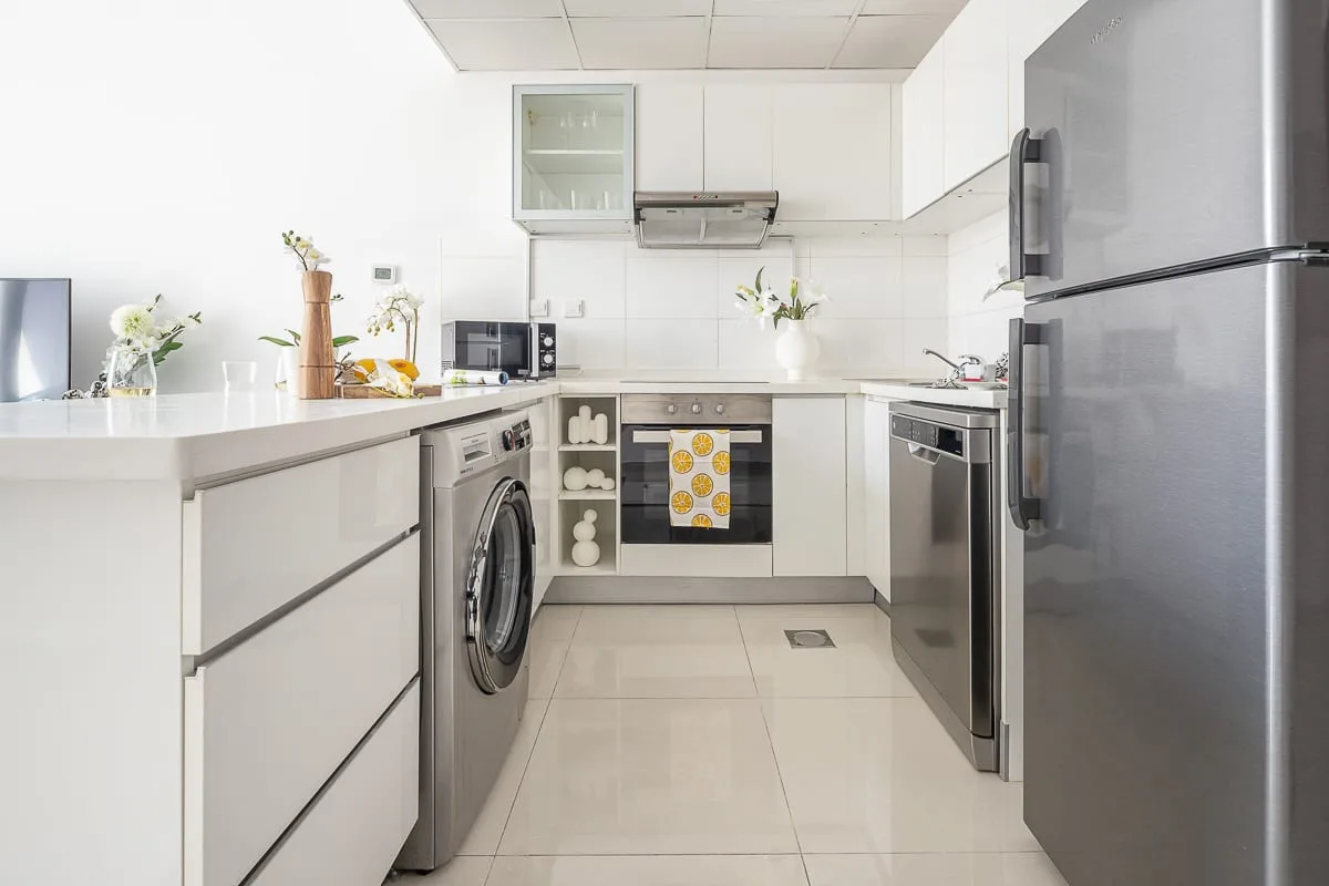 Una cocina luminosa con gabinetes blancos, electrodomésticos de acero inoxidable y suelo de baldosas.