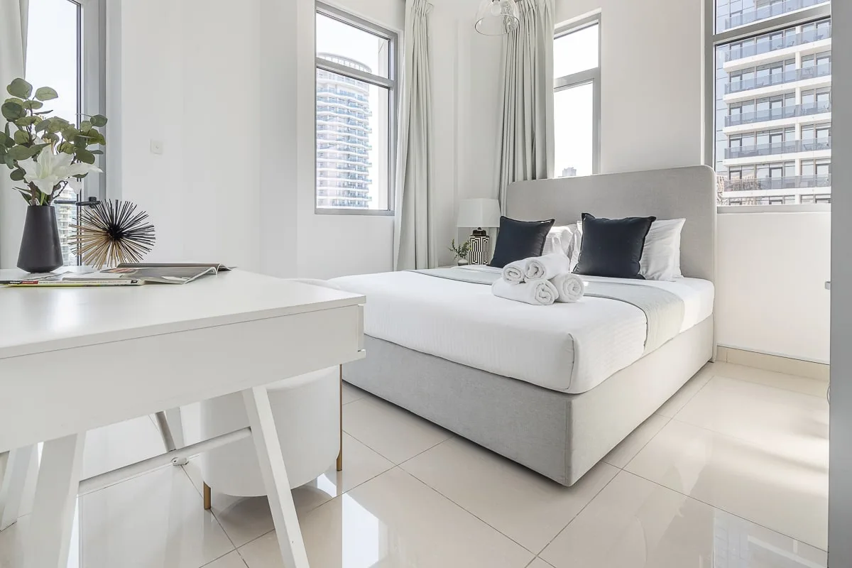 Un dormitorio luminoso con una cama bien arreglada junto a un escritorio blanco.