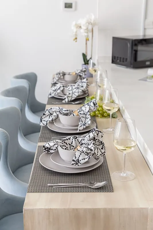 Una barra de comedor está preparada con platos, servilletas dobladas y copas de vino.