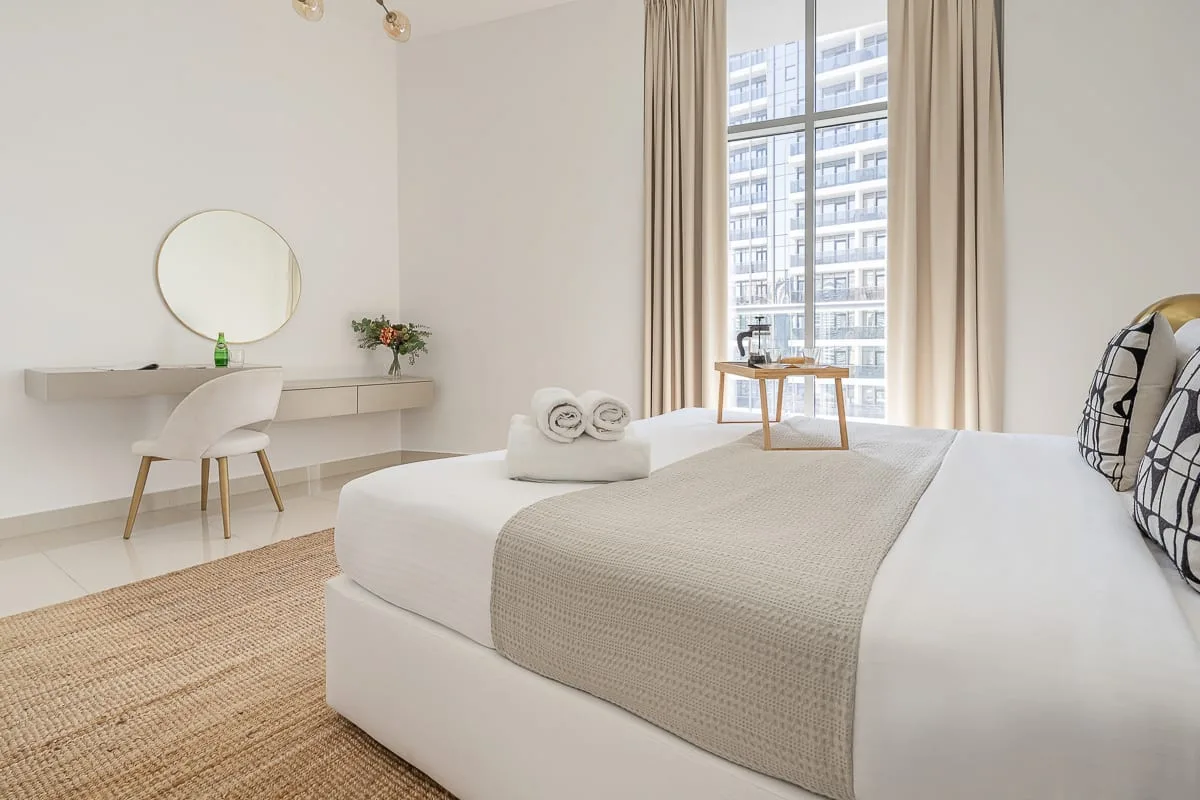 Un dormitorio luminoso con una cama bien arreglada y un escritorio junto a la ventana.