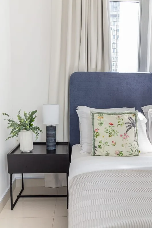 Un dormitorio con una cama bien tendida, un cojín floral y una mesita de noche.