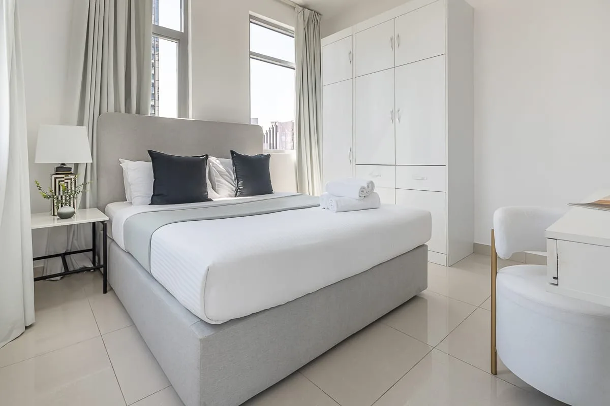 Un dormitorio luminoso con una cama tendida y ventanas altas.