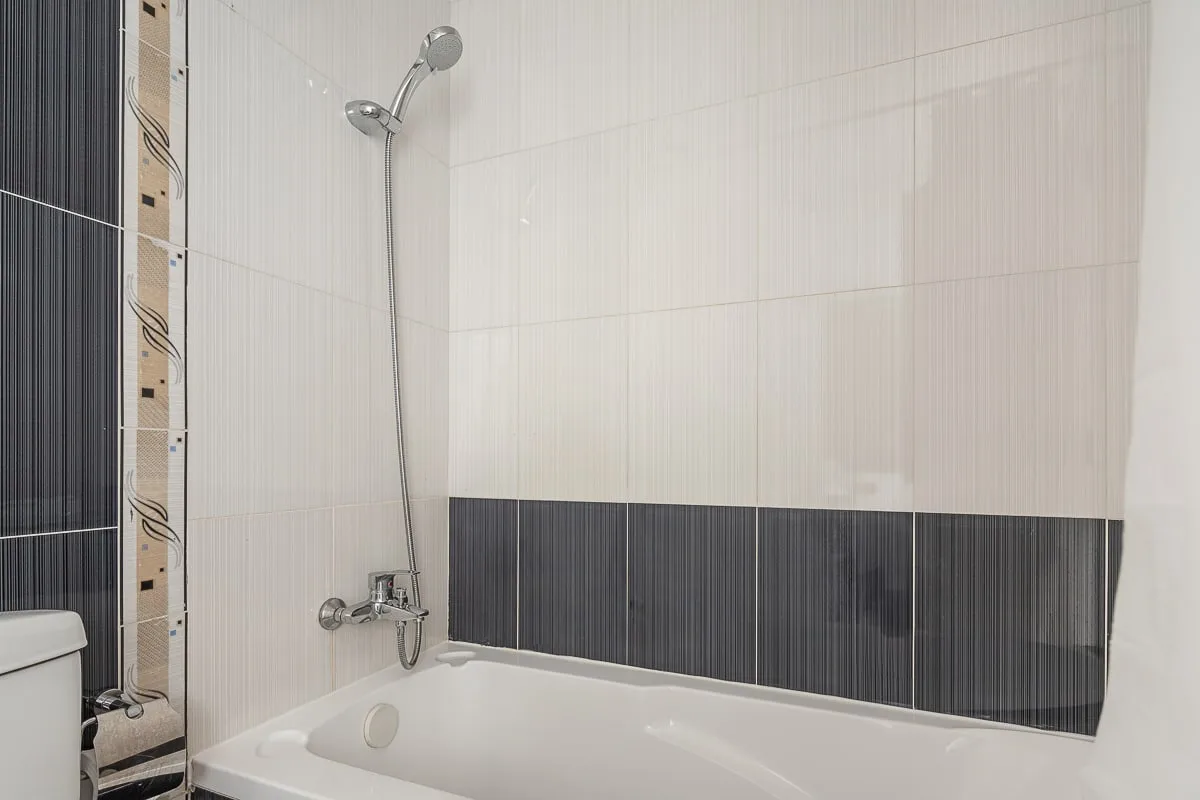 Un baño alicatado con bañera y ducha montada en la pared.