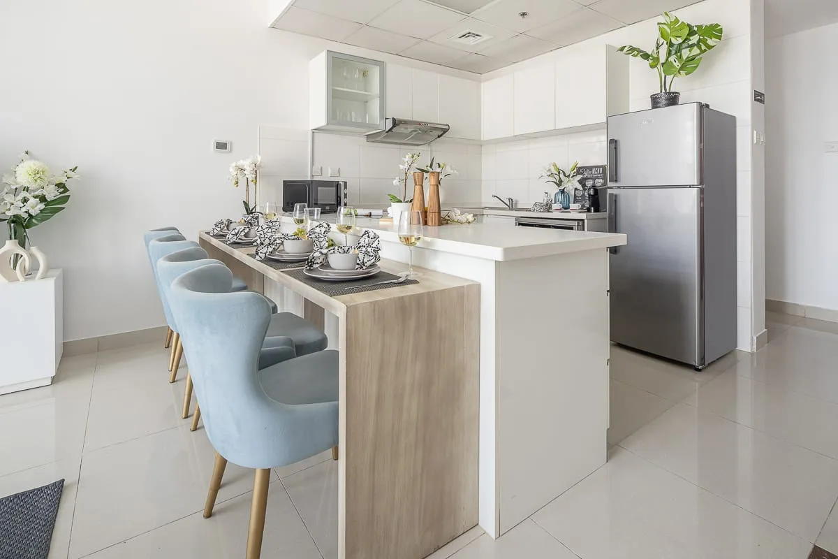 Una cocina luminosa con isla de comedor, asientos azul claro y refrigerador.