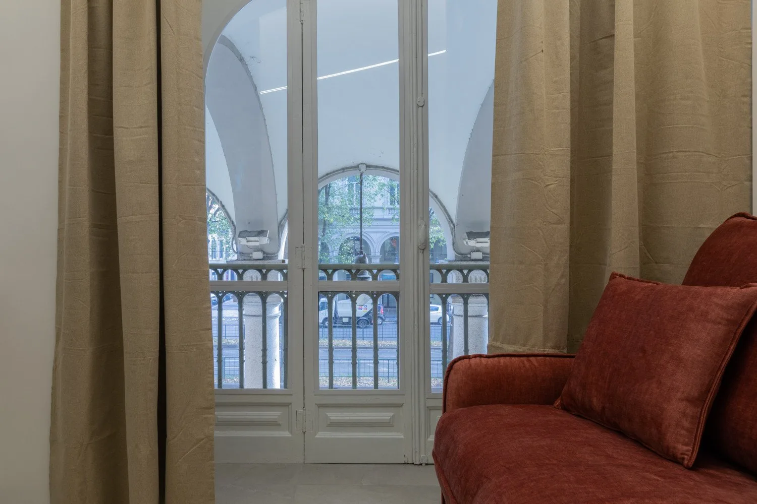A seating area beside tall curtained windows overlooking an arched balcony.