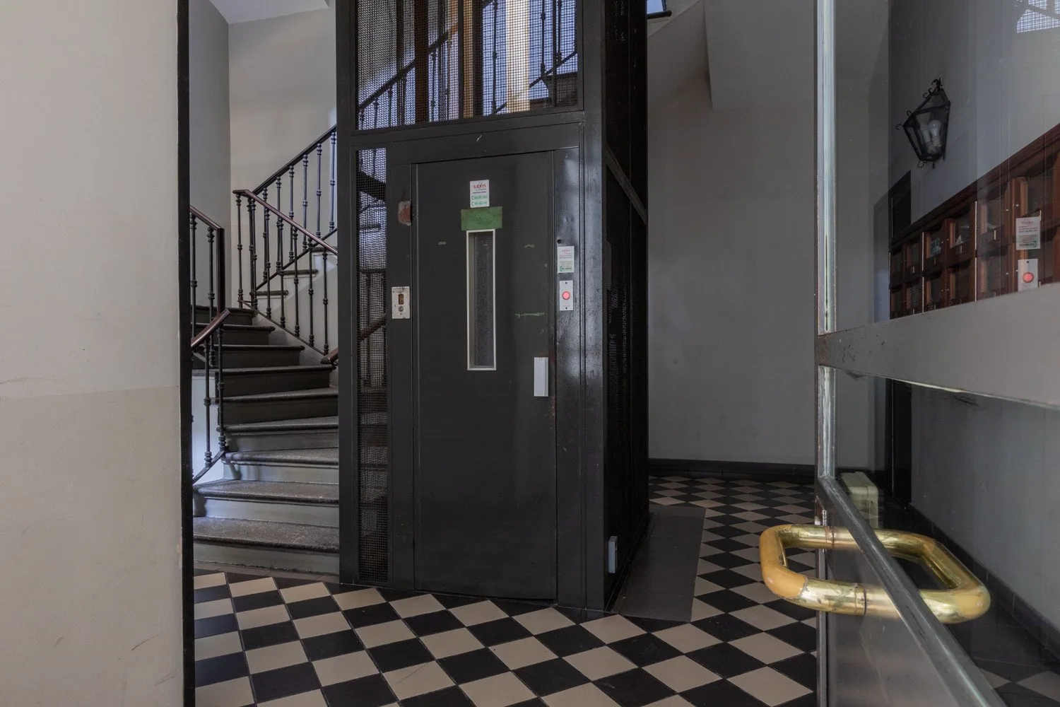 An interior entry hall with a dark elevator, staircase, and checkered floor.