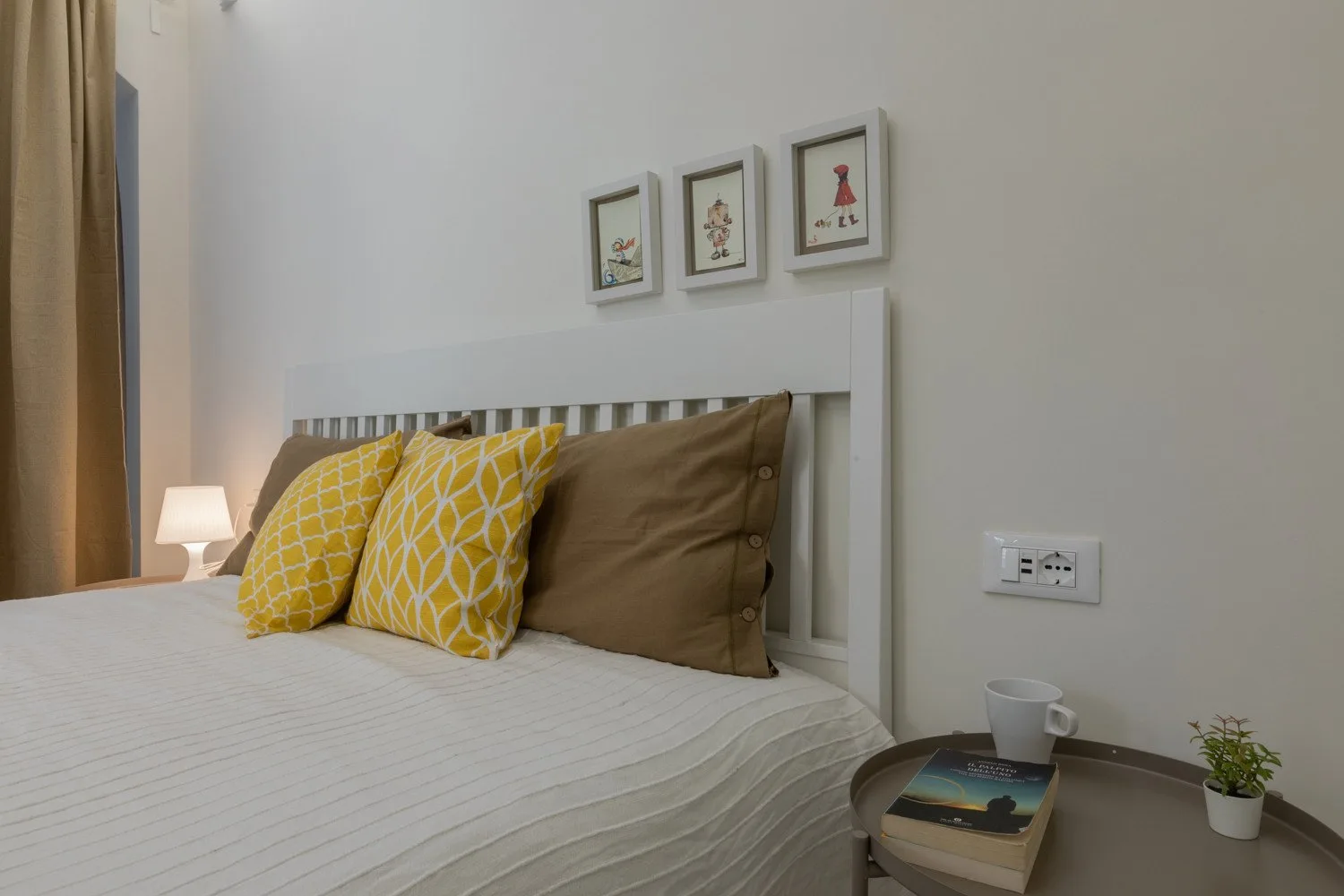 A bedroom with a neatly made bed, patterned pillows, and framed pictures above the headboard.