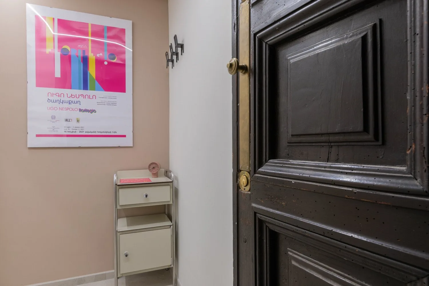 An entryway with a dark paneled door and a small cabinet beneath a wall poster.