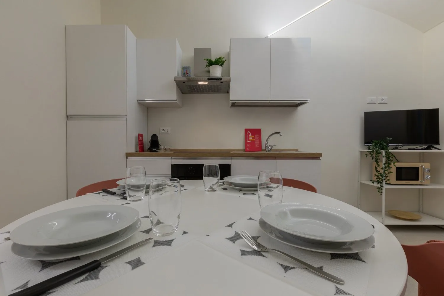 A dining area with a table set with dishes in front of a compact kitchen.