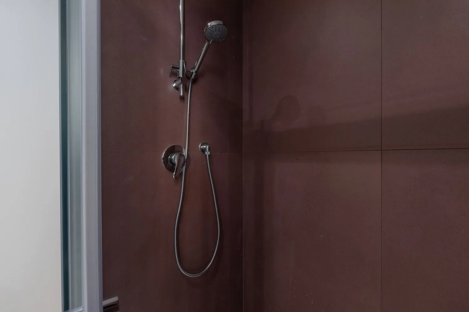 A shower with a handheld showerhead against dark reddish-brown wall panels.