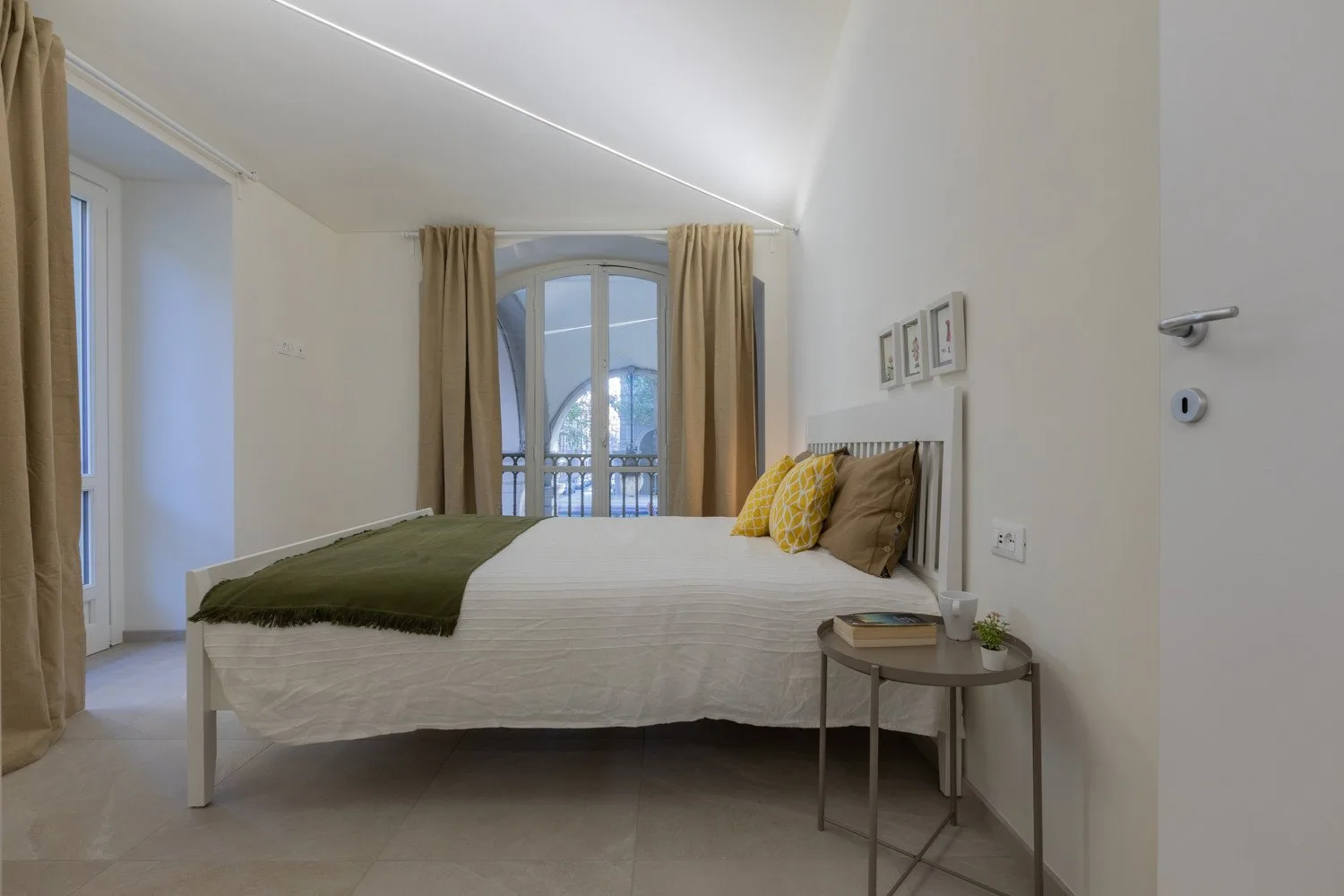 Un dormitorio con cama, mesita de noche y ventana arqueada con cortinas.