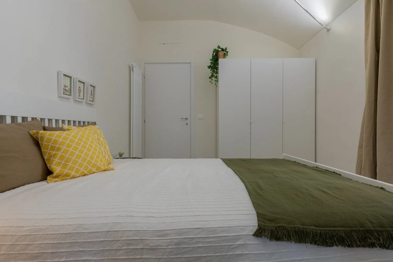 A bedroom with a bed, a wardrobe, and a small potted plant.
