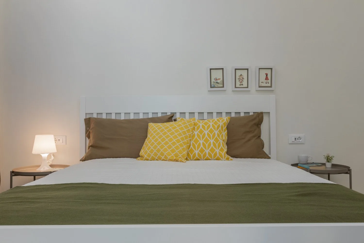 A bedroom with a neatly made bed, patterned pillows, and a bedside lamp.