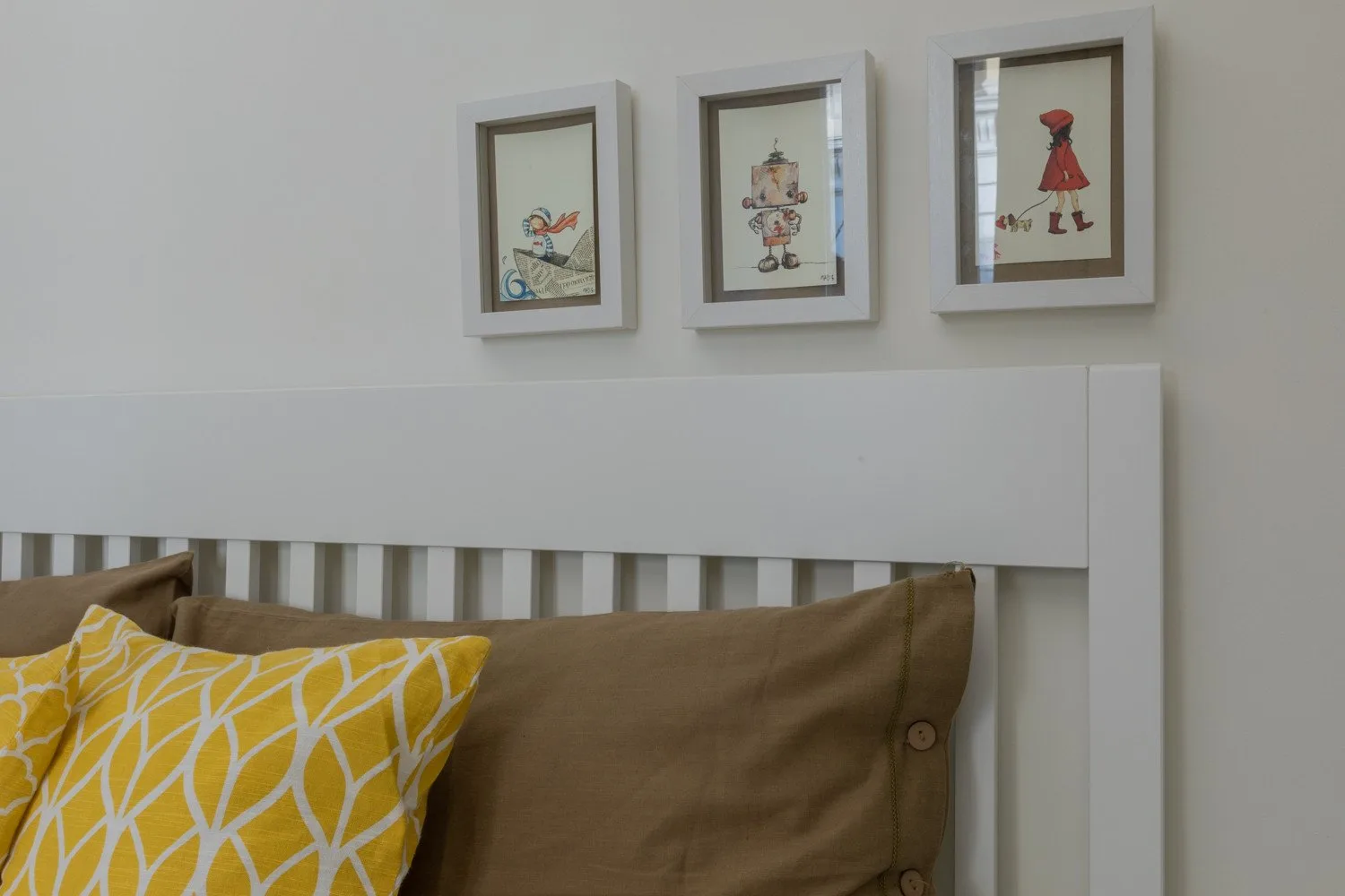 Una cama con cojines amarillos estampados está debajo de ilustraciones enmarcadas.