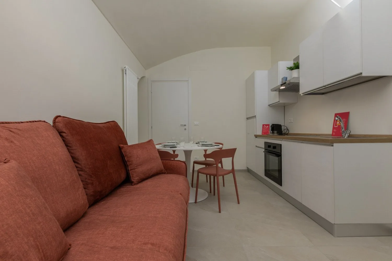 A compact living and kitchen area with a rust-colored sofa and dining table.