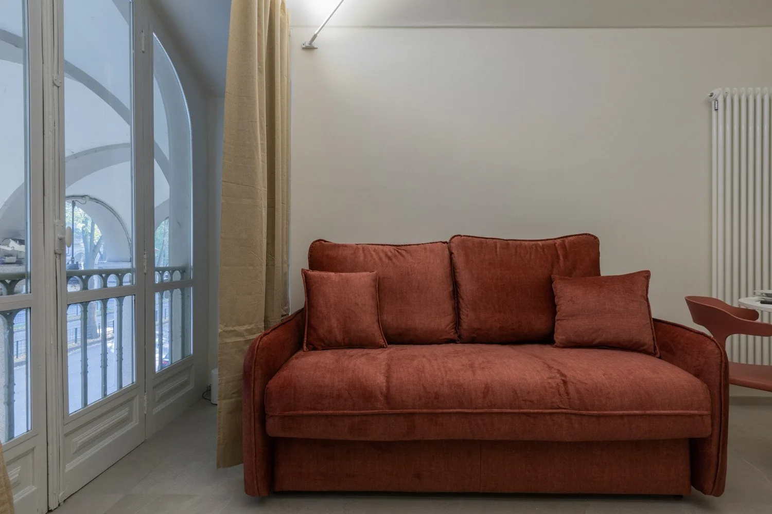 A living room with a rust-colored sofa beside tall arched windows.