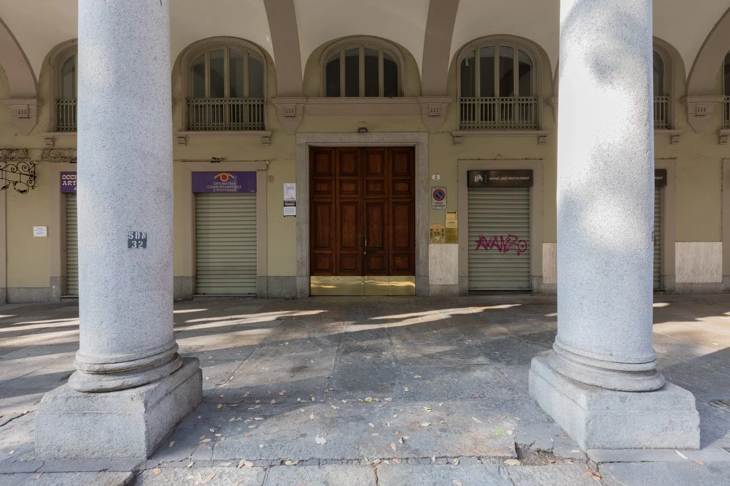 A building entrance with a wooden double door and shuttered storefronts beneath arched windows.
