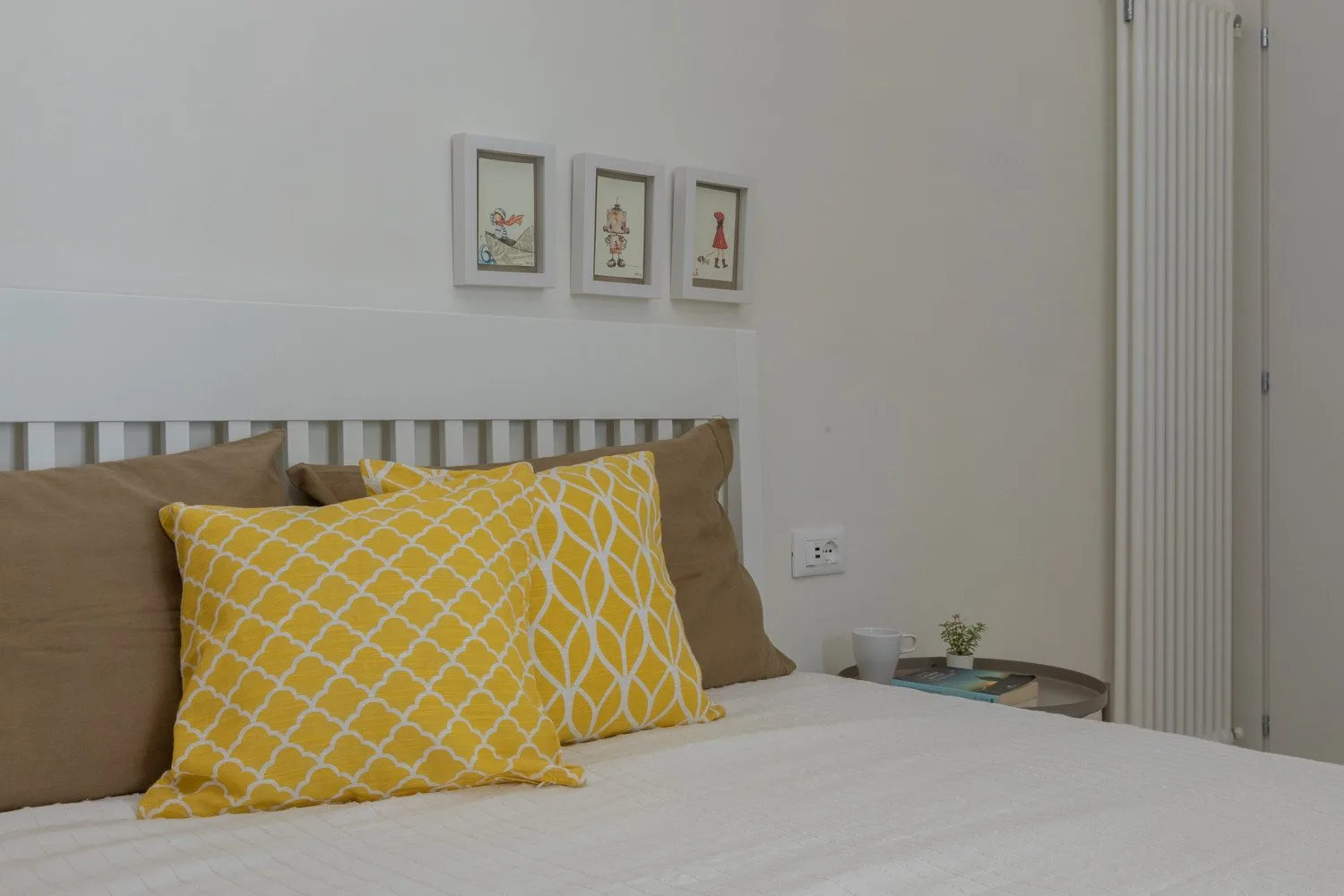 A bedroom with a bed, yellow patterned pillows, and framed pictures on the wall.