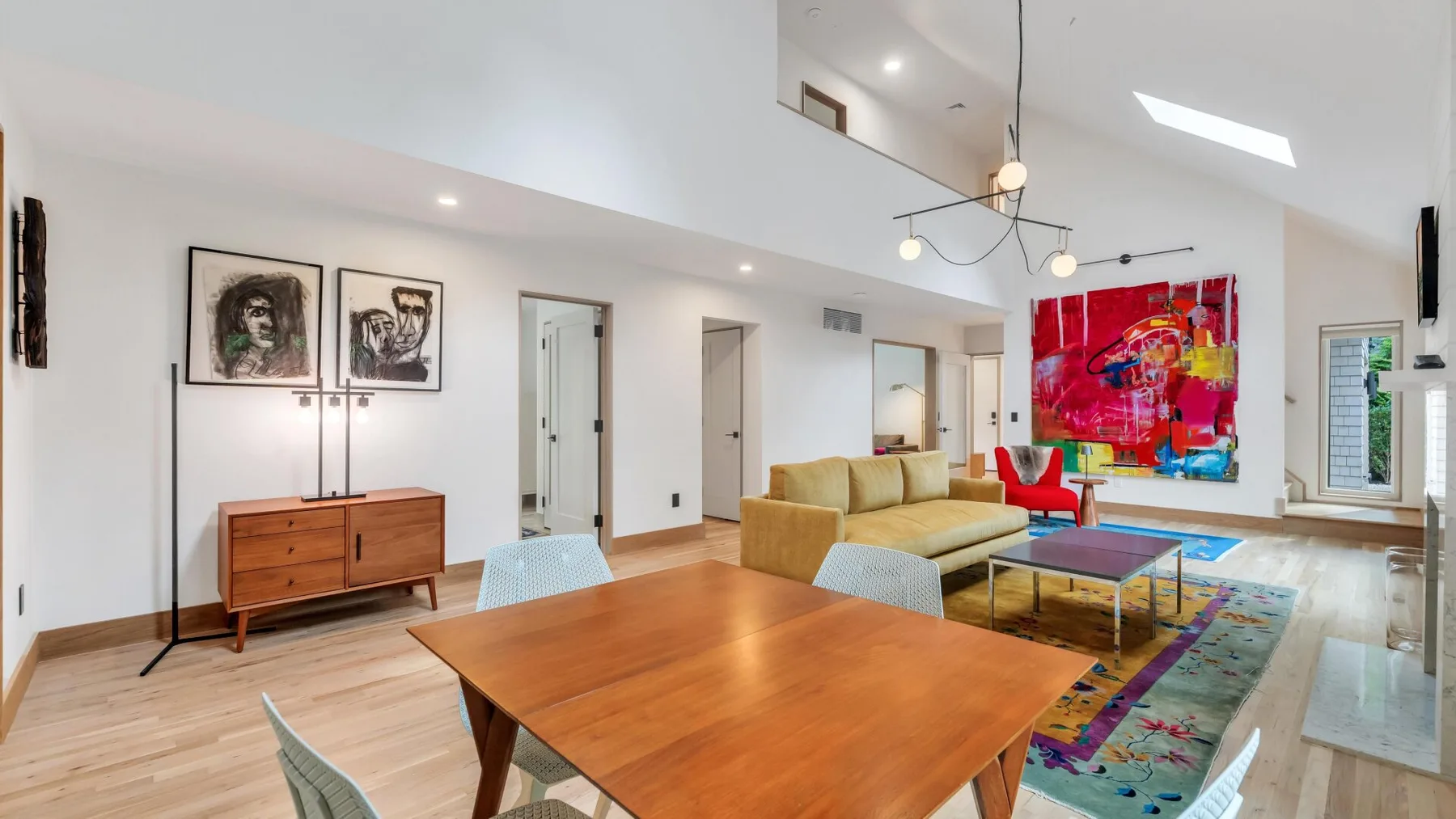 A bright open living and dining area with a wooden table and colorful artwork.