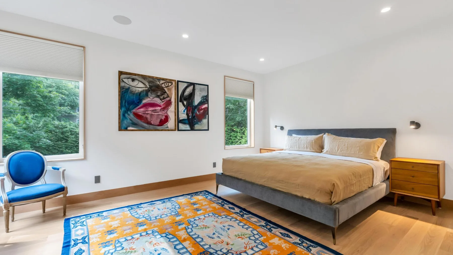 A bright bedroom with a large bed, colorful rug, and windows overlooking greenery.
