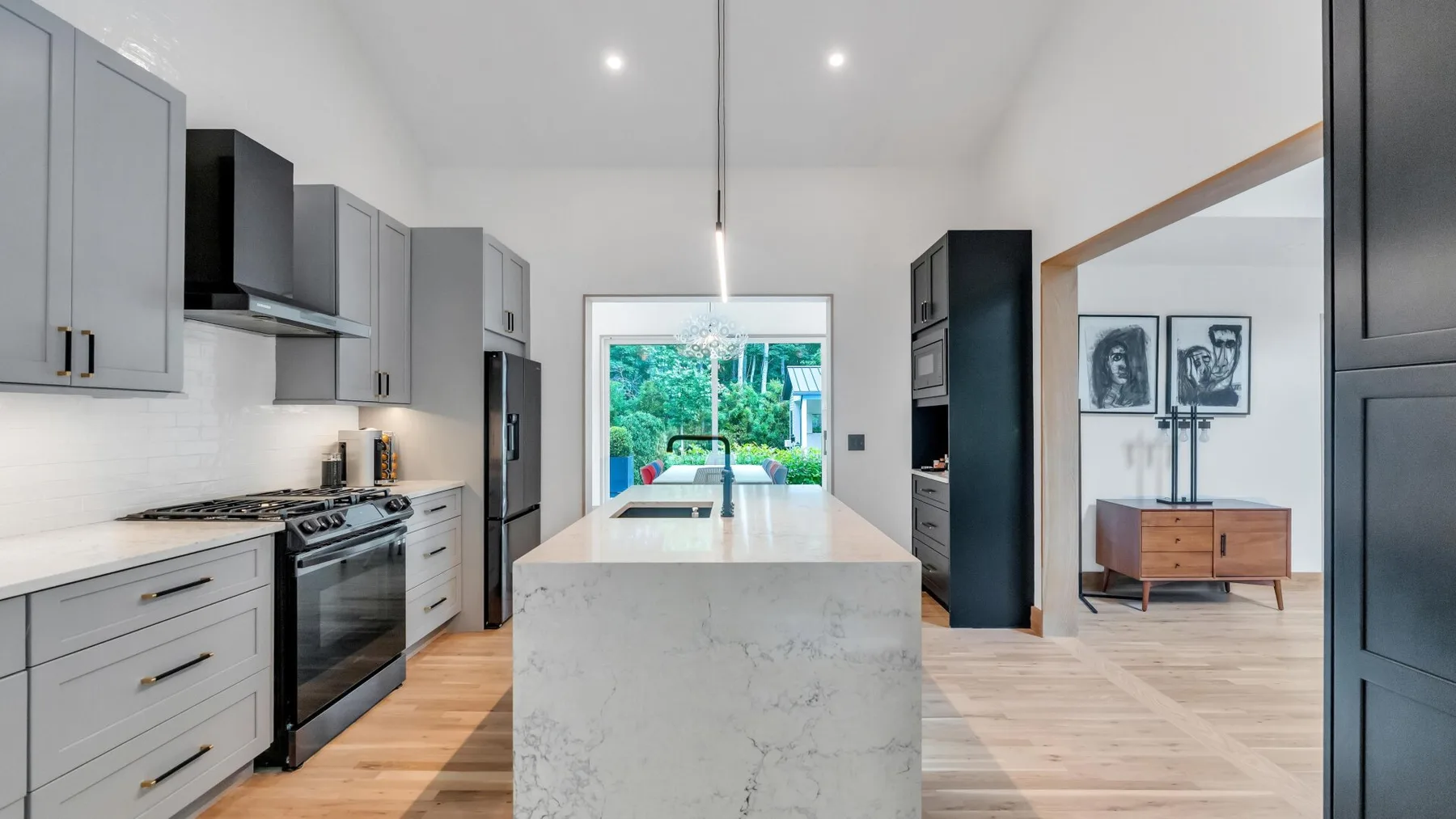 A modern kitchen with a large island opens onto a bright living area.