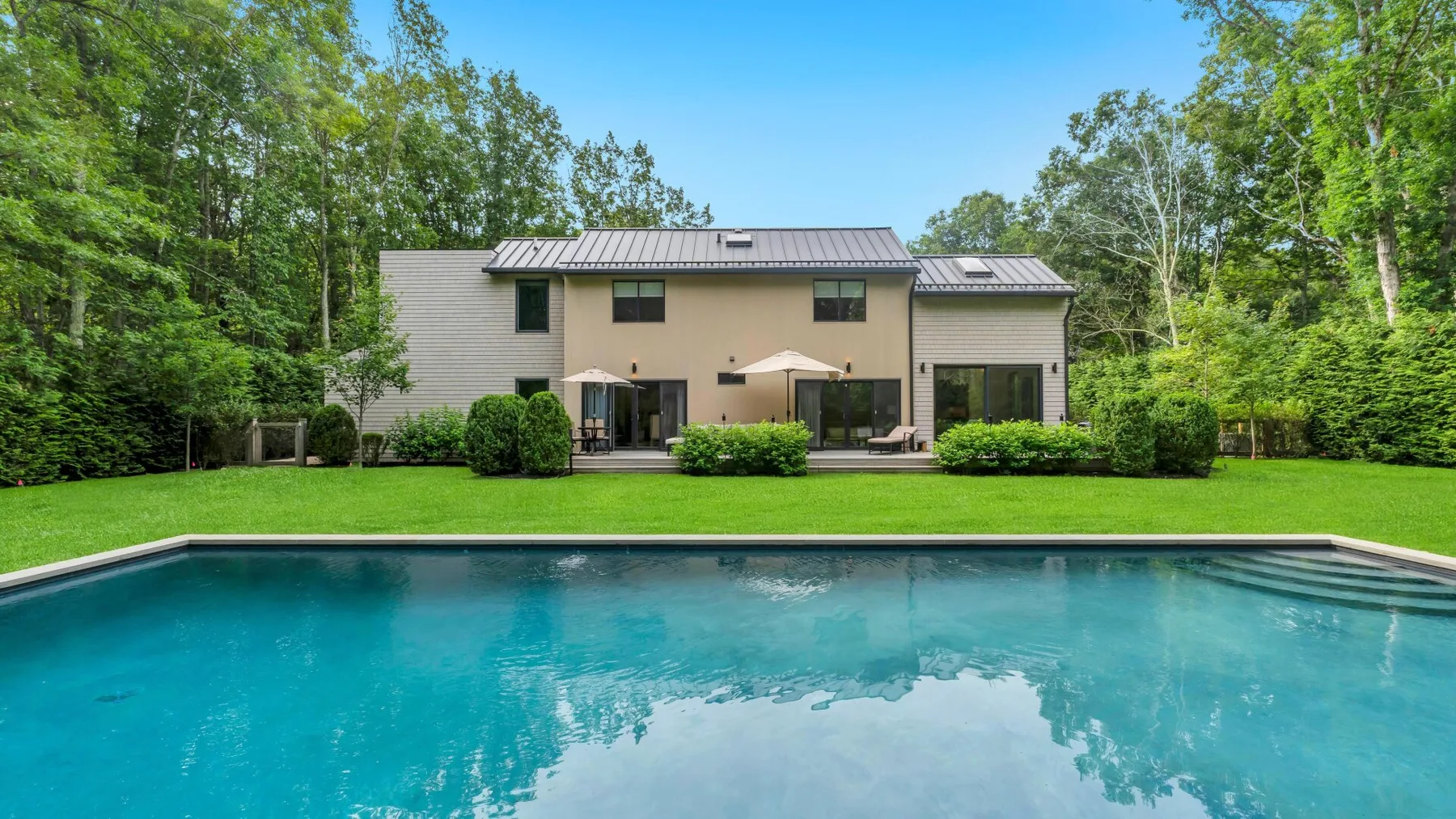 A modern house overlooks a swimming pool and broad green lawn.
