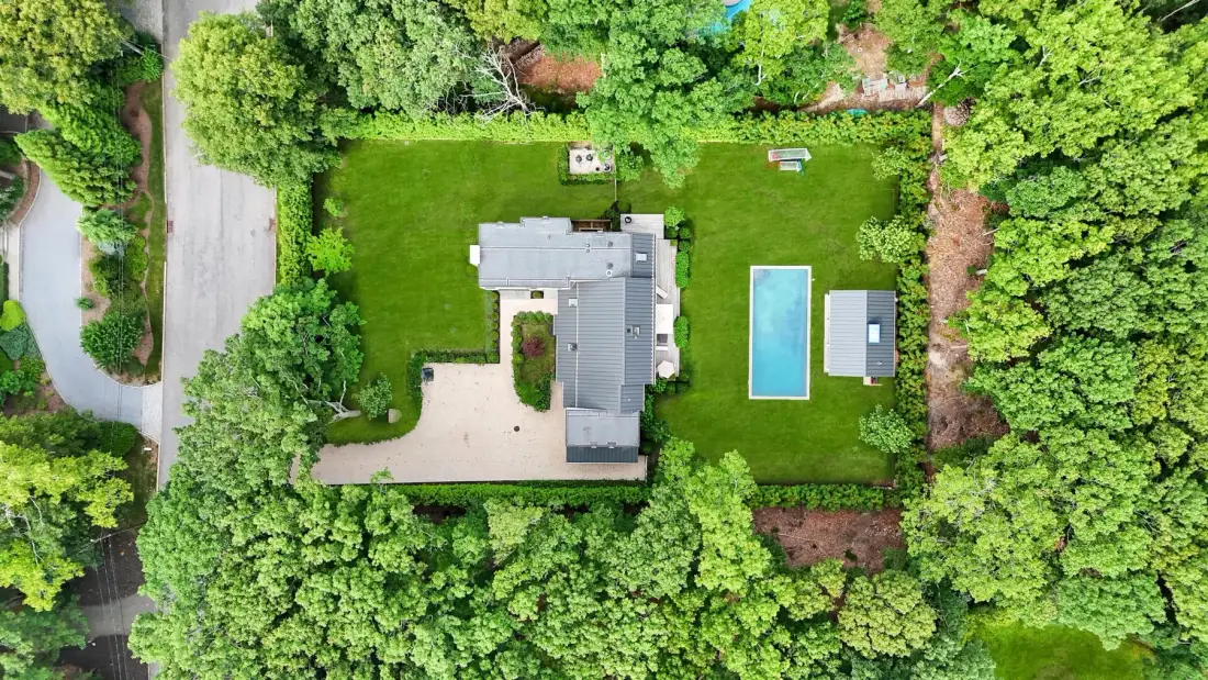 An aerial view shows a house, a swimming pool, and a lawn surrounded by trees.