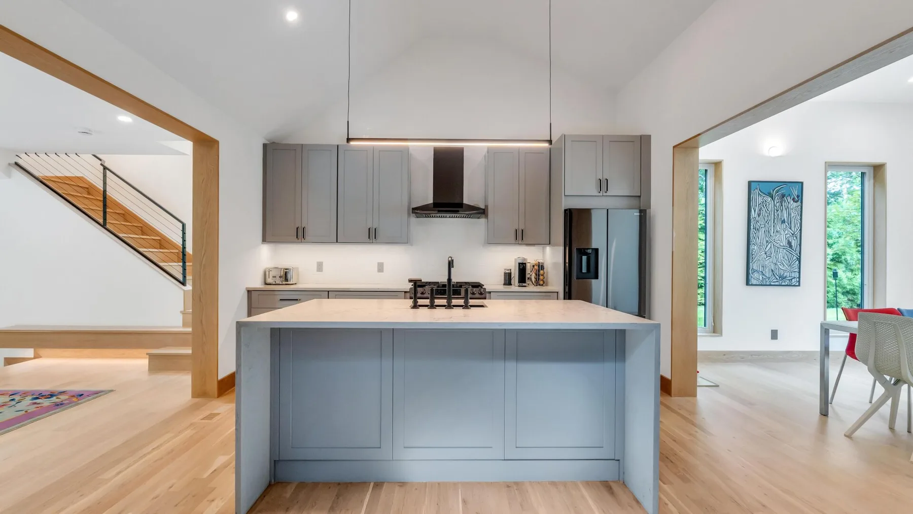A bright kitchen with a central island and gray cabinets opens onto adjacent rooms.