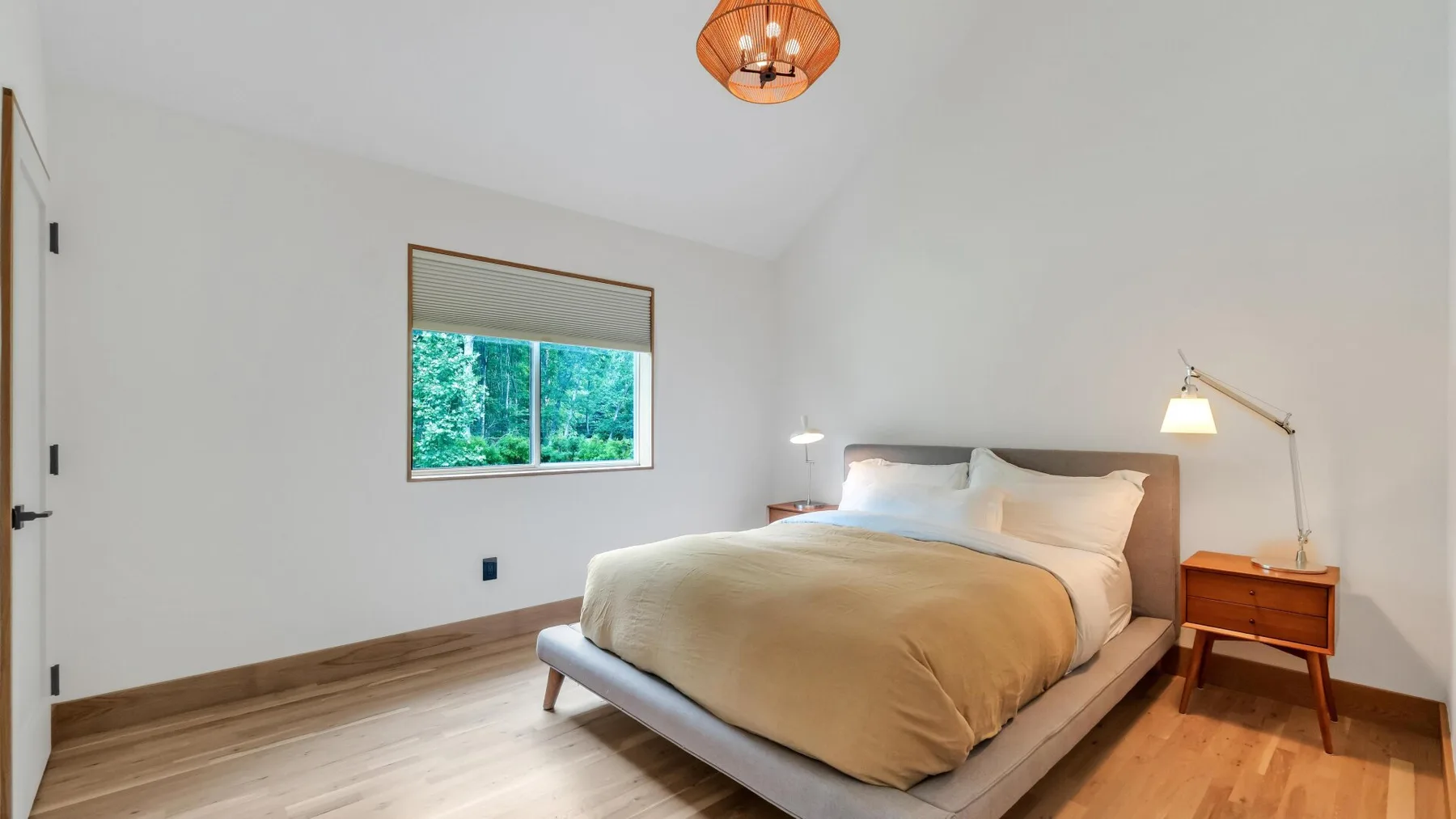 A bright bedroom with a bed, bedside table, and large window.