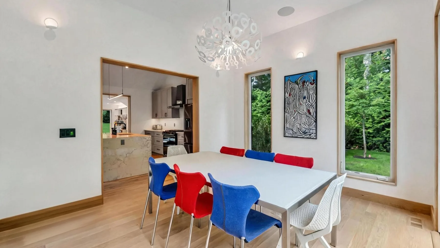 A dining area with a white table and colorful chairs beside large windows.
