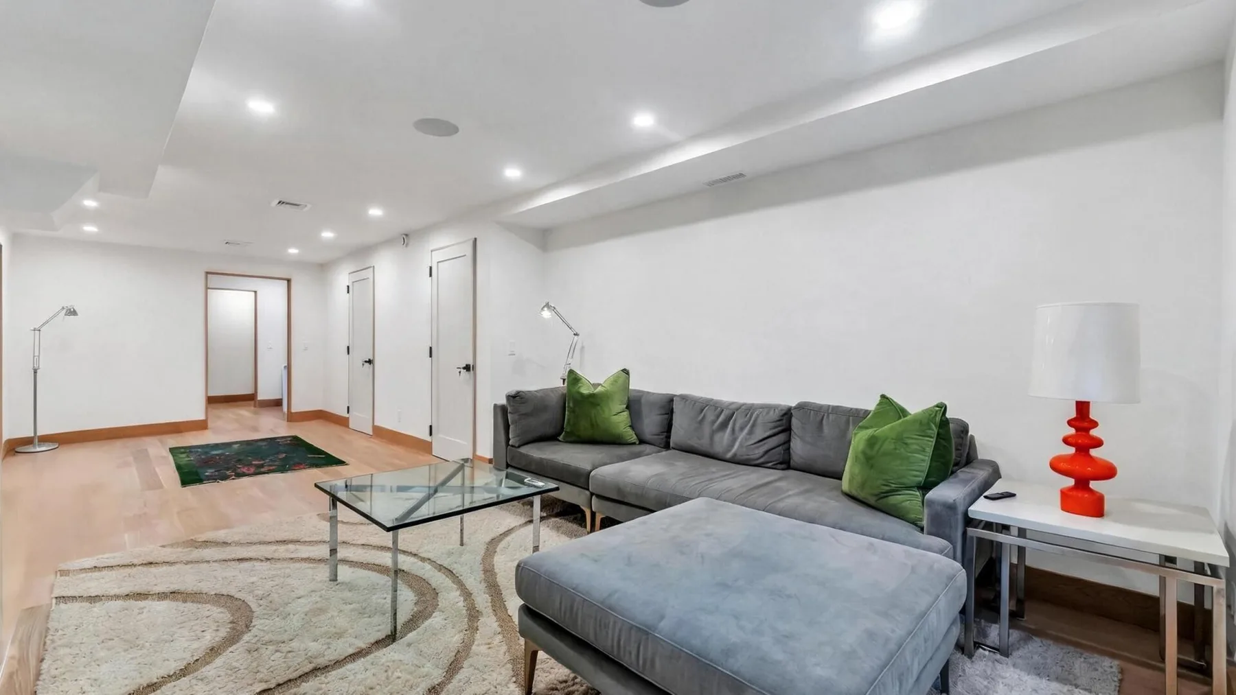 A bright living room with a gray sectional, green cushions, and a glass coffee table.