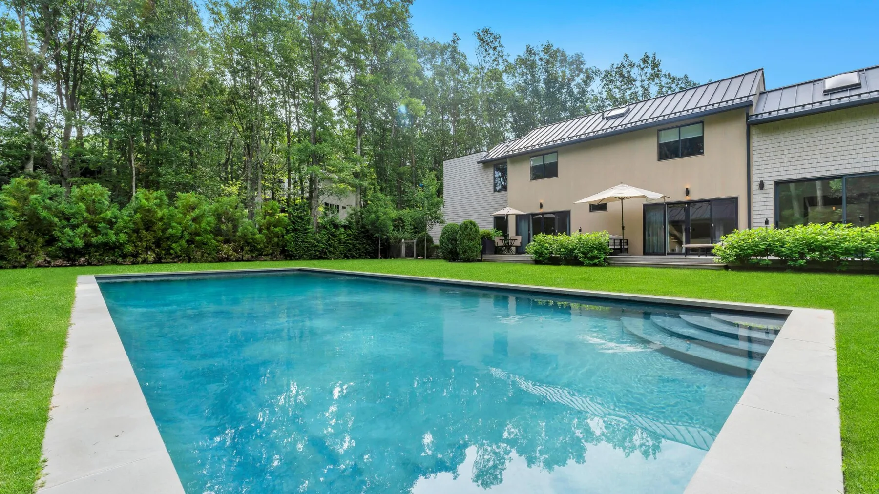 Una piscina está junto a una casa moderna y un césped verde.