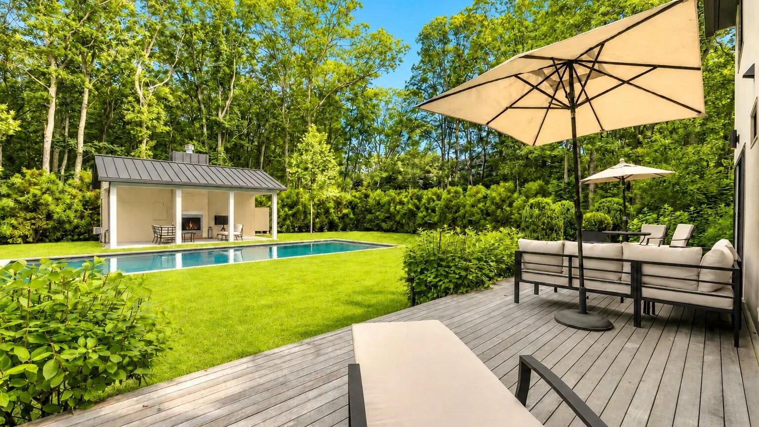 An outdoor deck overlooks a lawn, swimming pool, and small poolside building.