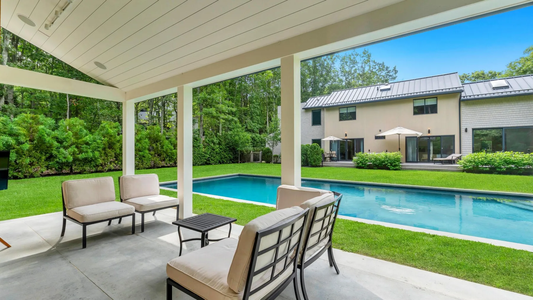 A covered patio overlooks a swimming pool and a modern house.