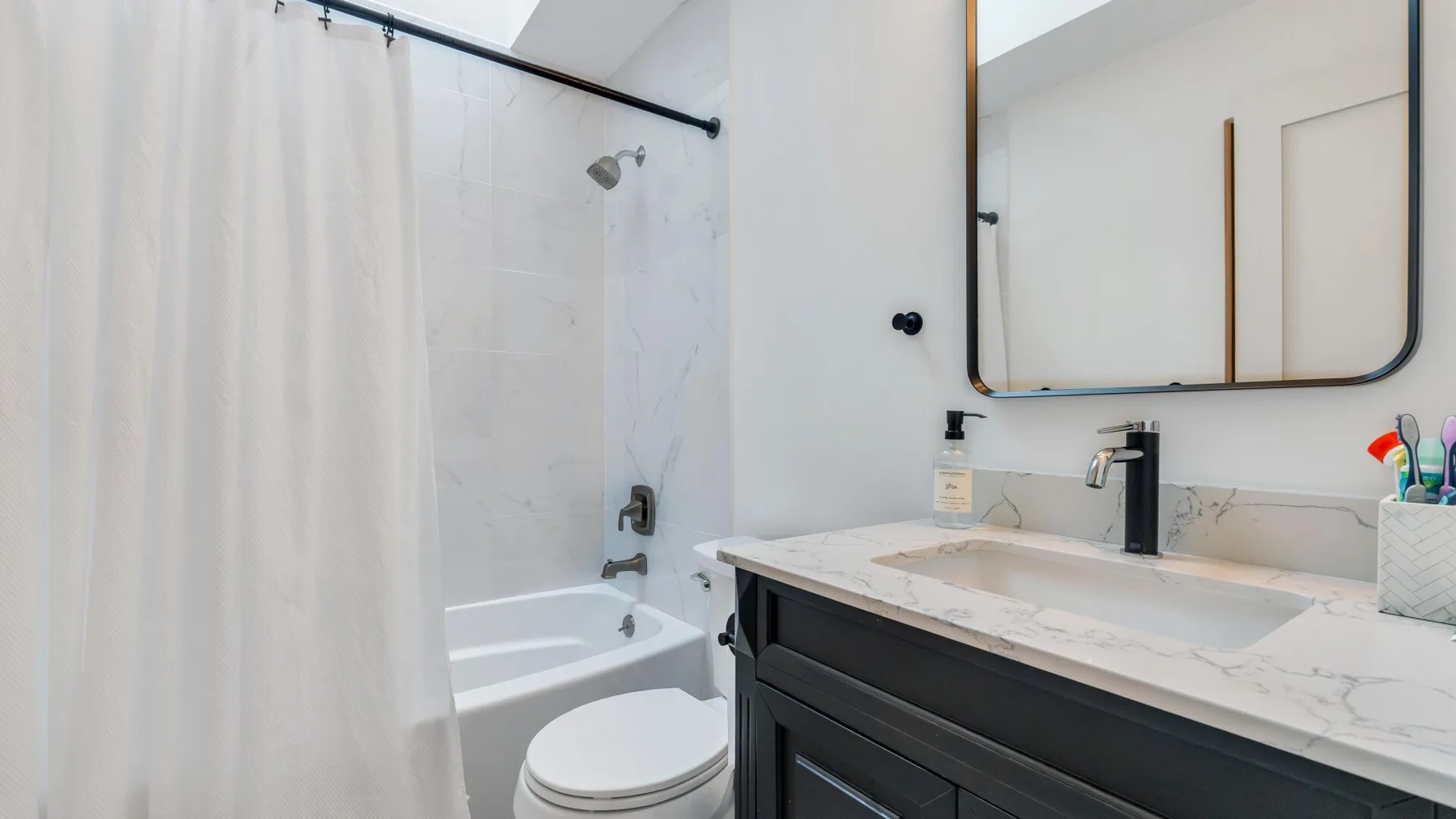 A bathroom with a bathtub, shower curtain, and sink vanity.