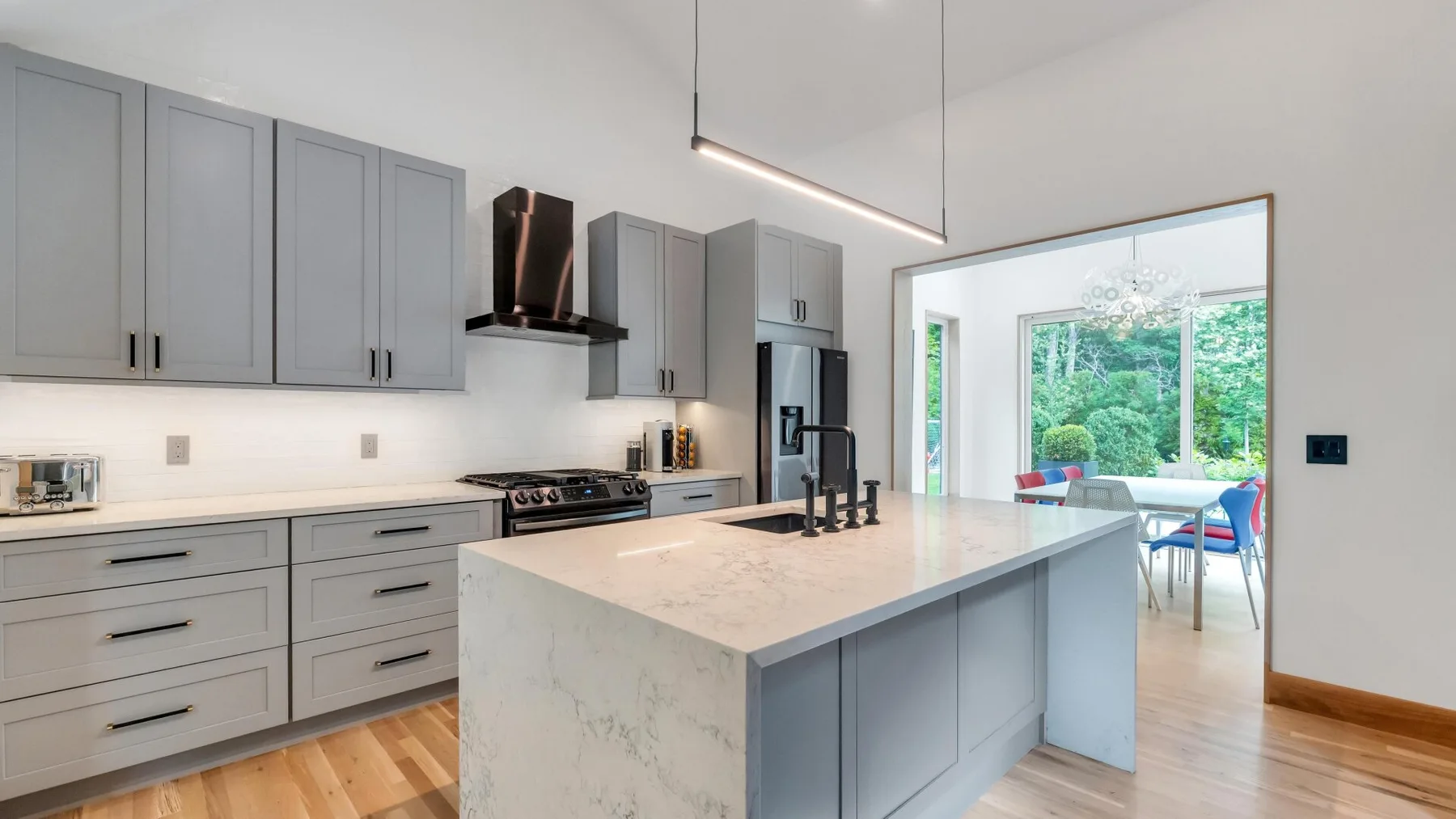 A modern kitchen with gray cabinets and a large island opens onto a dining area.