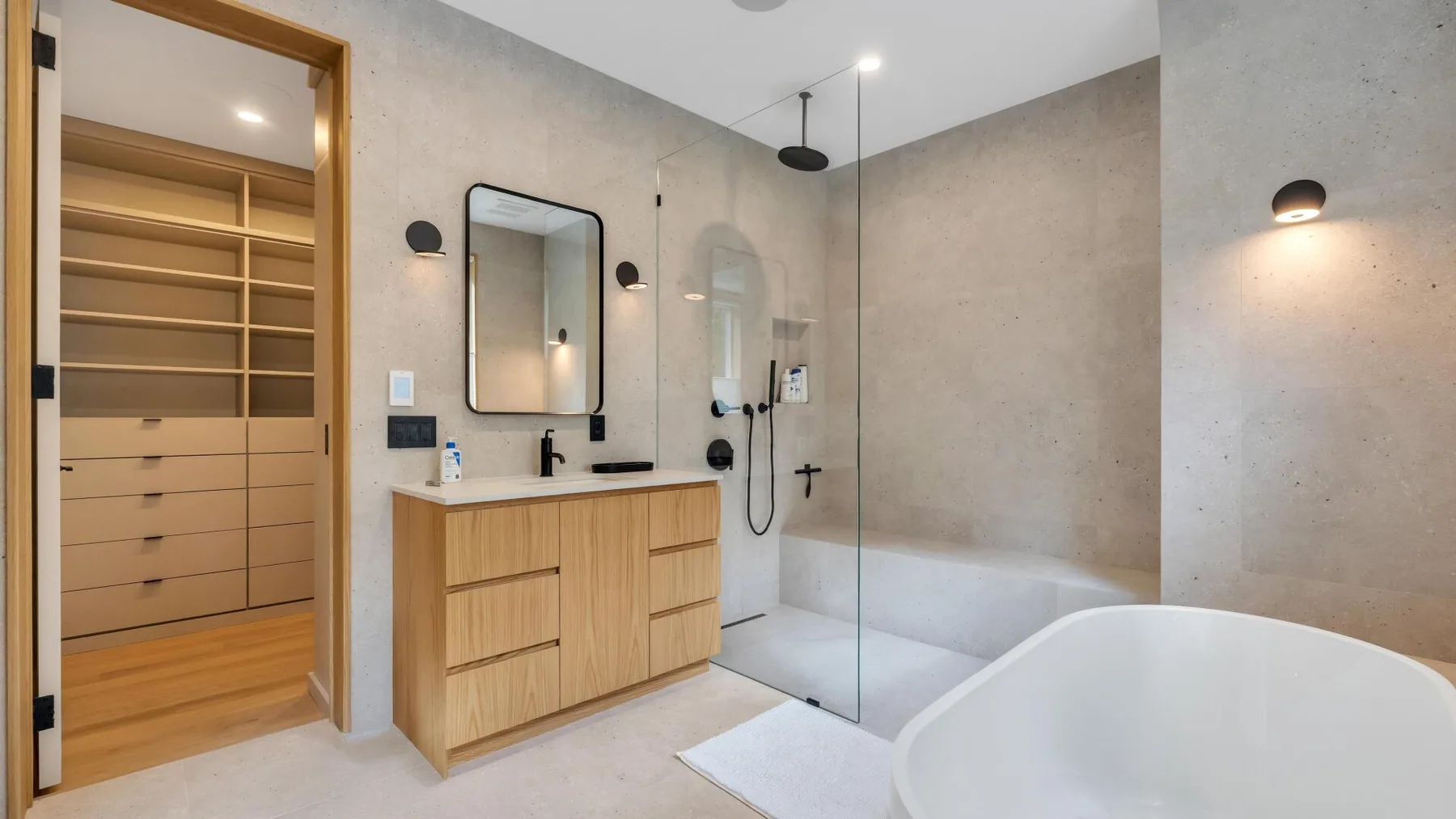 A bathroom with a wood vanity, glass shower screen, and freestanding bathtub.