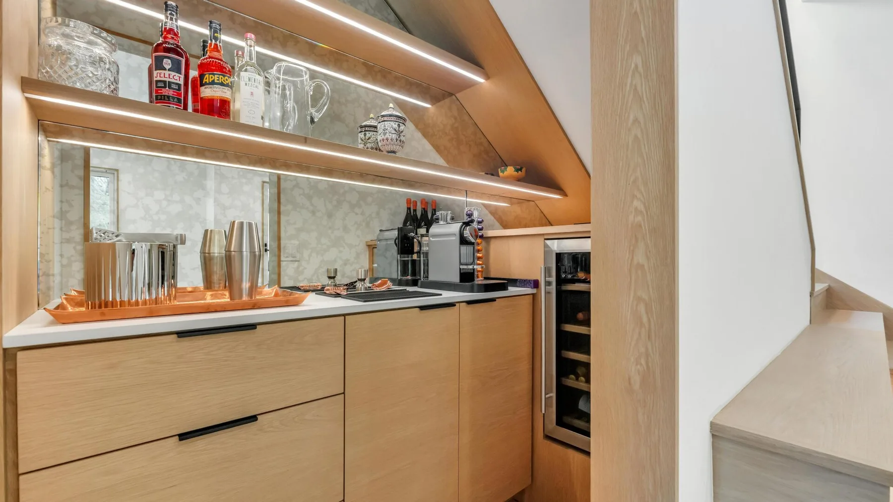 A modern kitchen with a countertop coffee machine and illuminated display shelves.