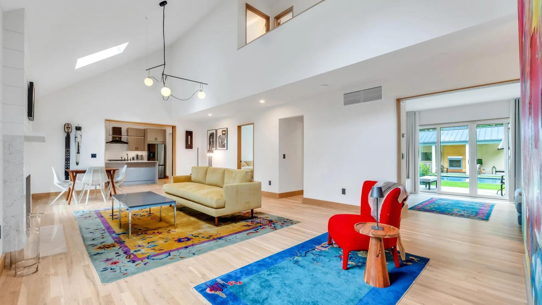 A bright living room with colorful rugs, a sofa, and red seating.
