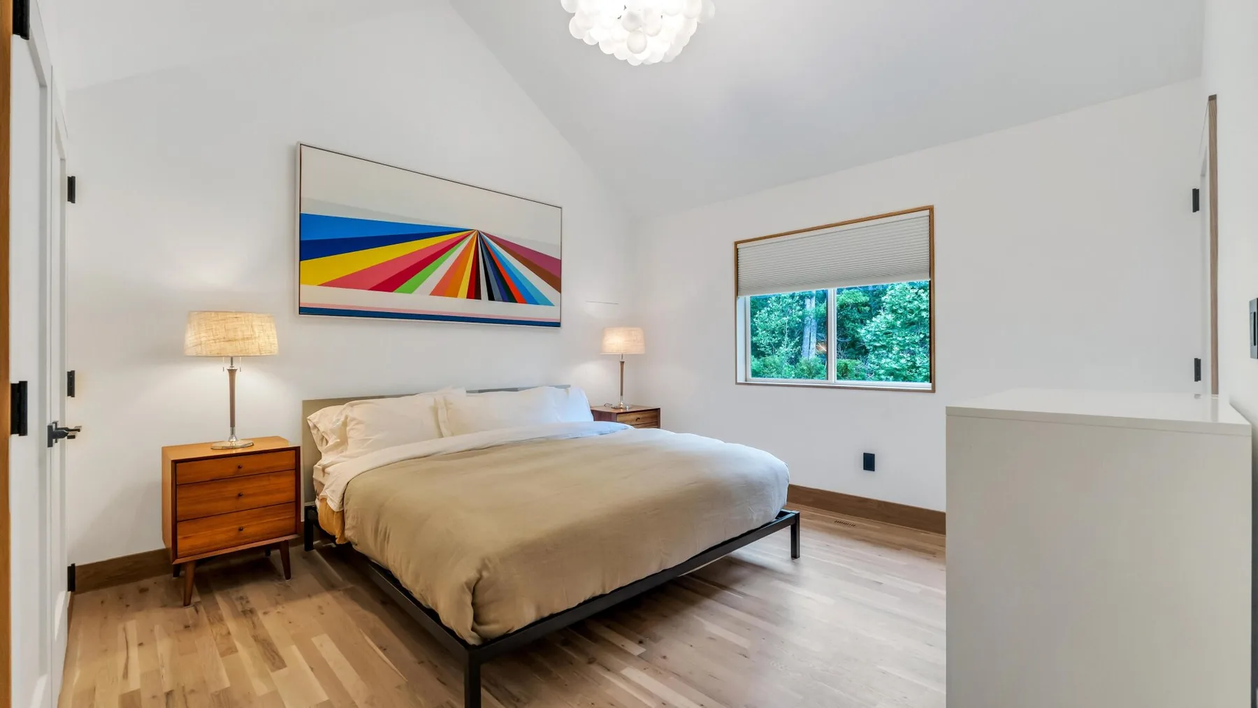 A bright bedroom with a double bed, bedside tables, and colorful wall art.