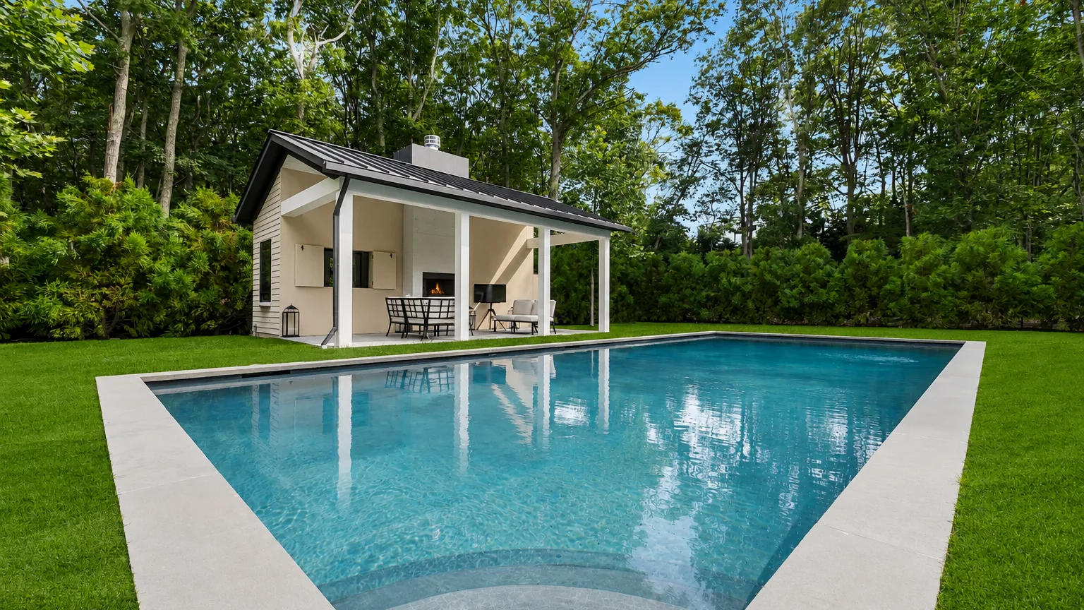 A swimming pool sits beside a modern pavilion in a wooded garden.