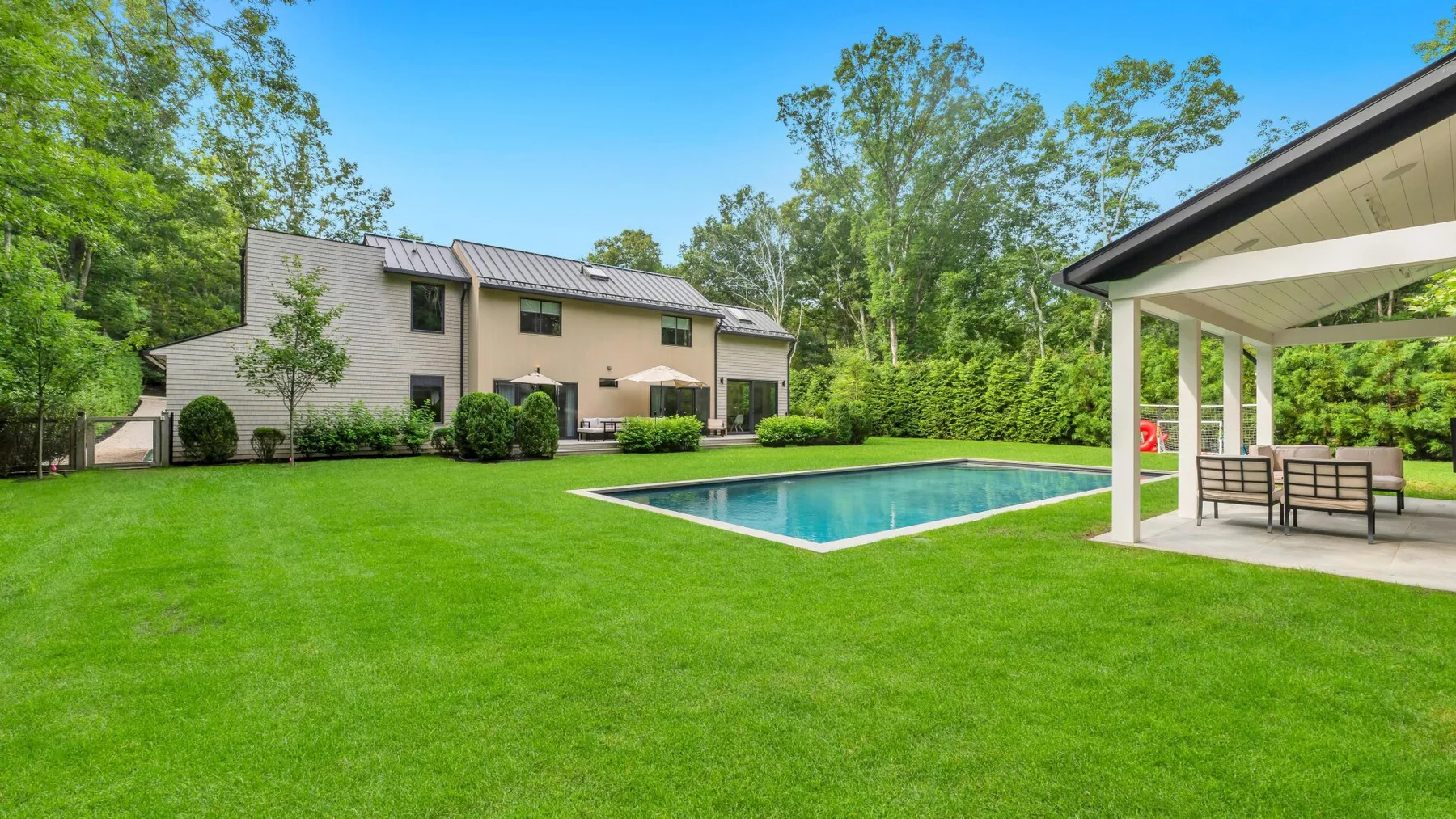 A backyard with a swimming pool, lawn, and covered patio.