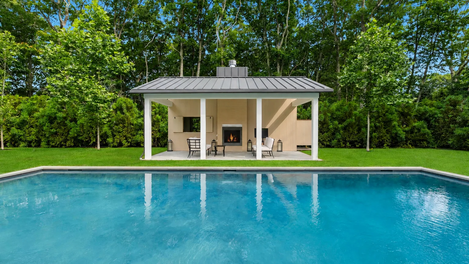 A swimming pool faces an open-sided pavilion with seating.
