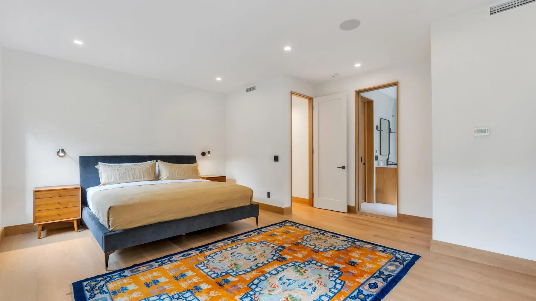 A bedroom with a bed, bedside table, and colorful patterned rug.